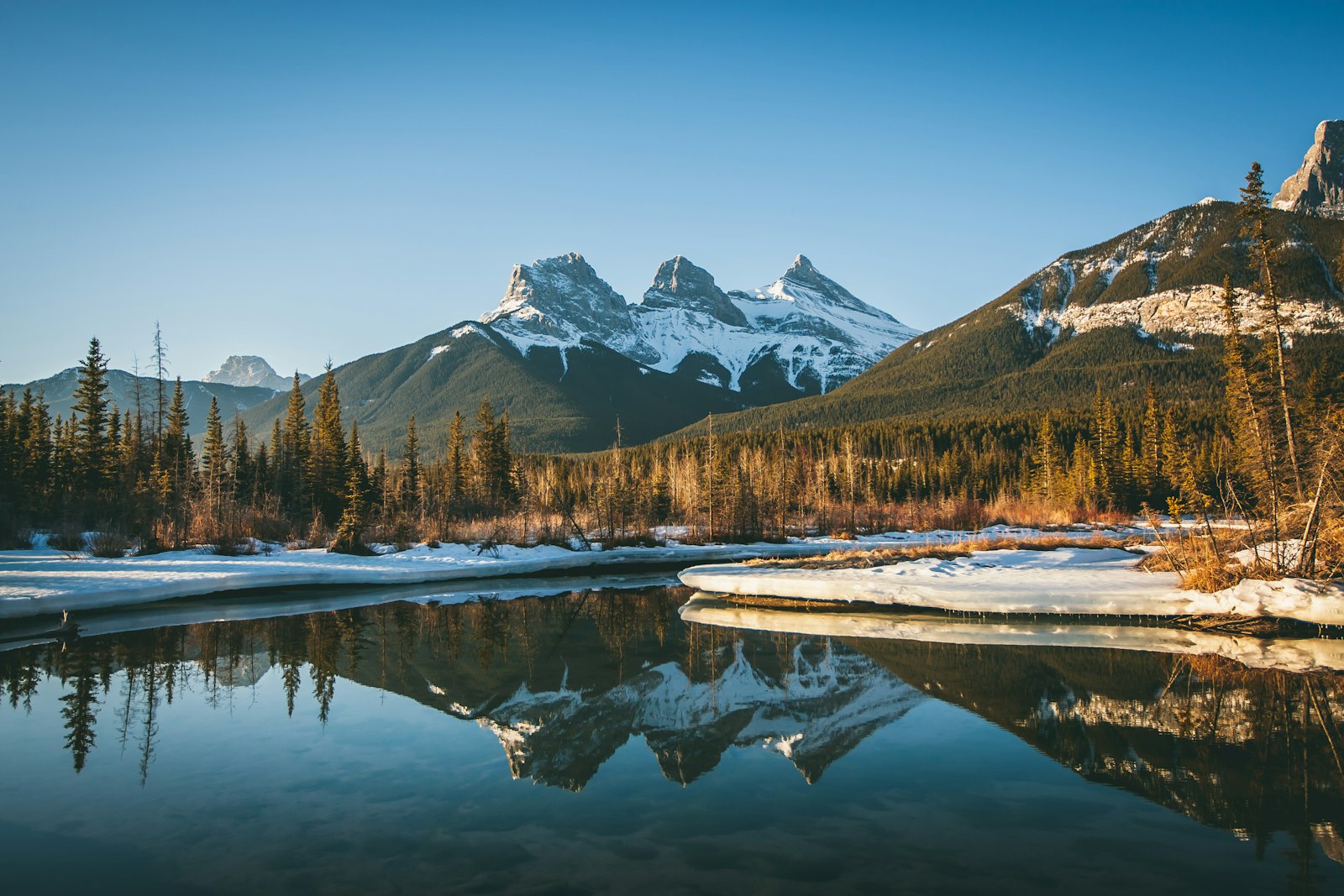 Three Sisters mountains reflected in the river near Canmore
